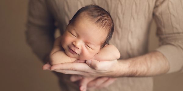 dad holding newborn baby boy on his hand with in a mocha color background