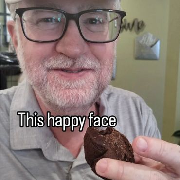 Older man smiling while holding a chocolate muffin with caption 'This happy face'.