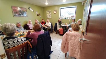 A group of elderly women gathered around tables in a cozy, small room.