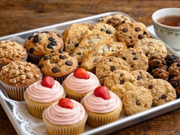 Tray of assorted baked goods including cupcakes, muffins, and cookies with a cup of tea.