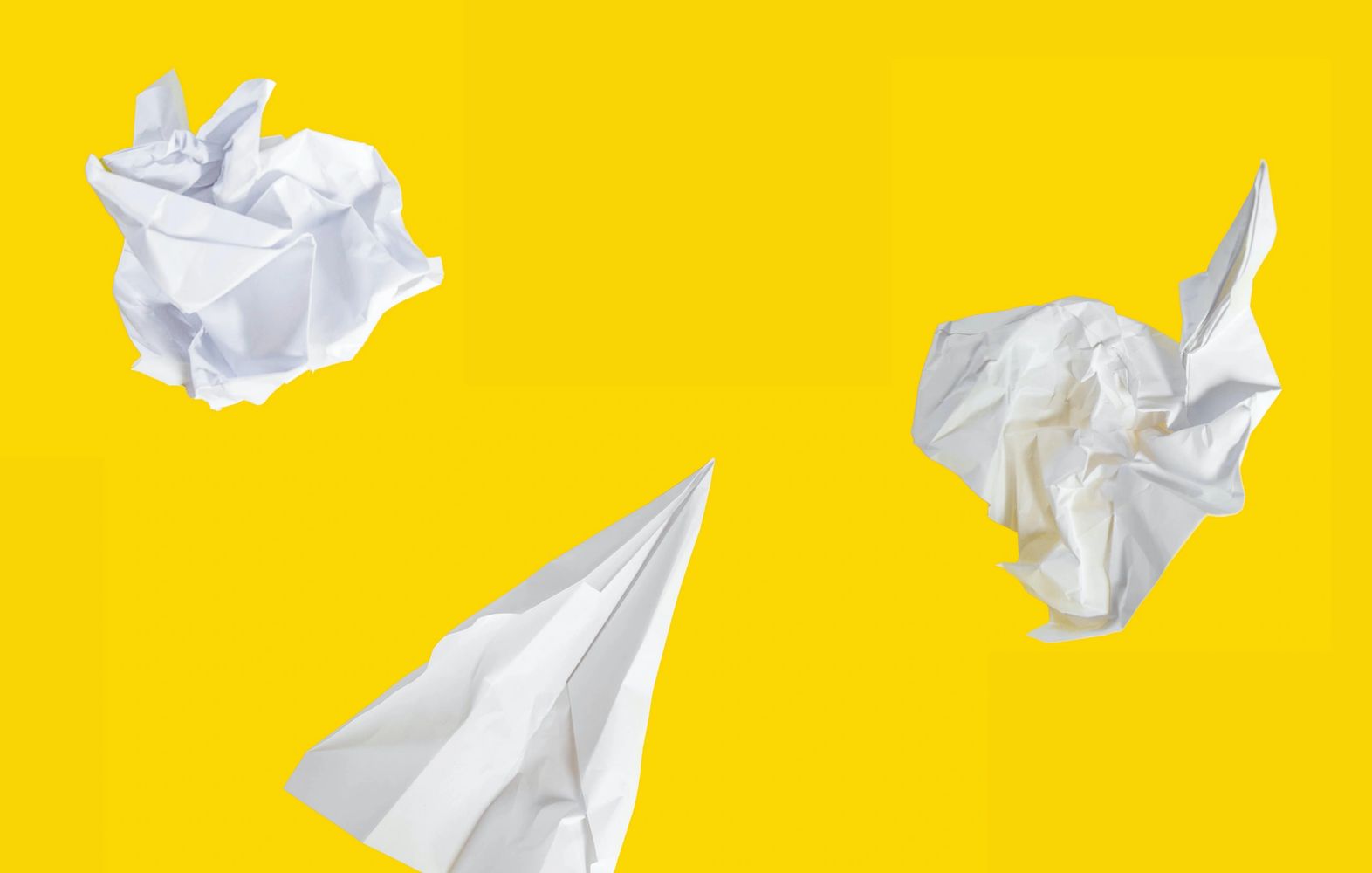 Two pieces of white, crumpled paper and a paper airplane on a yellow background.