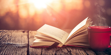 A book and cup of coffee on a table outside.