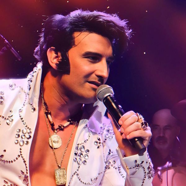 Performer in a studded white jacket singing into a microphone.