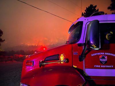 Fire truck at night with wildfire glowing in the background.
