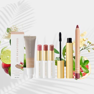 Assorted makeup products with natural fruit and floral elements in the background.
