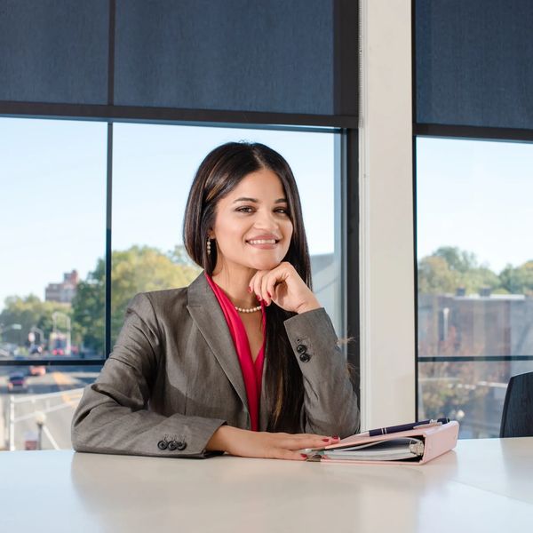 Confident woman in business attire sitting at a desk with a binder.