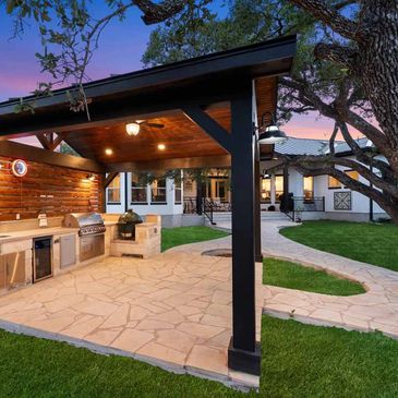 Outdoor kitchen and patio area under a wooden pergola with a scenic sunset.