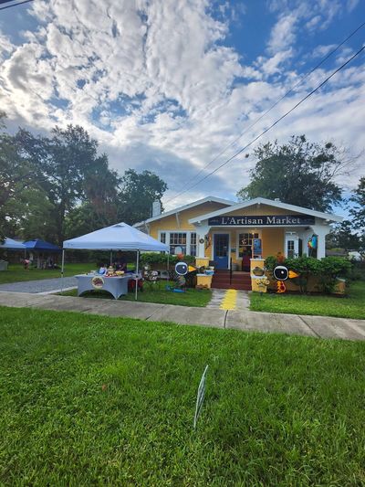 Sunny day at L'Artisan Market with a white canopy and vibrant yard decorations.