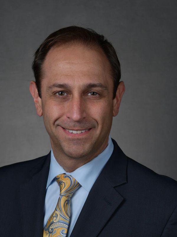 Professional headshot of a smiling man in a suit and patterned tie.