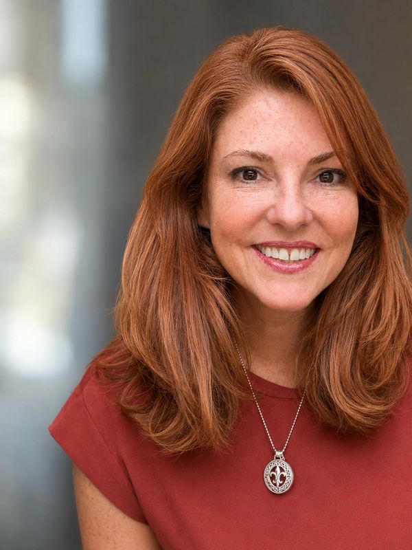 Smiling woman with red hair wearing a pendant necklace and red top.