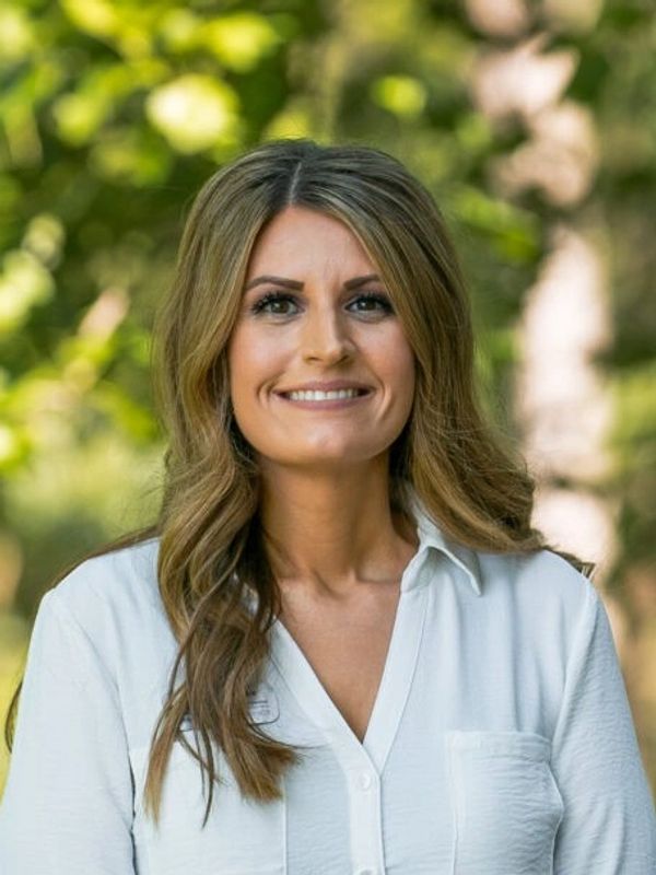 Smiling woman with long hair wearing a white shirt outdoors.