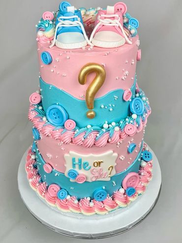 Two-Tier Gender Reveal Cake with Baby Shoes, Buttons, and Pearls. Layered Blue and Pink Cake Design.