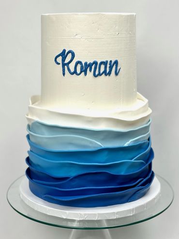 Two Tier White Birthday Cake with Ombre Blue to White Wave Design on Bottom Tier.