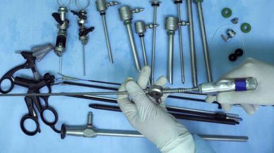 Surgical instruments and endoscopic tools arranged on a blue surface with gloved hands handling one tool.