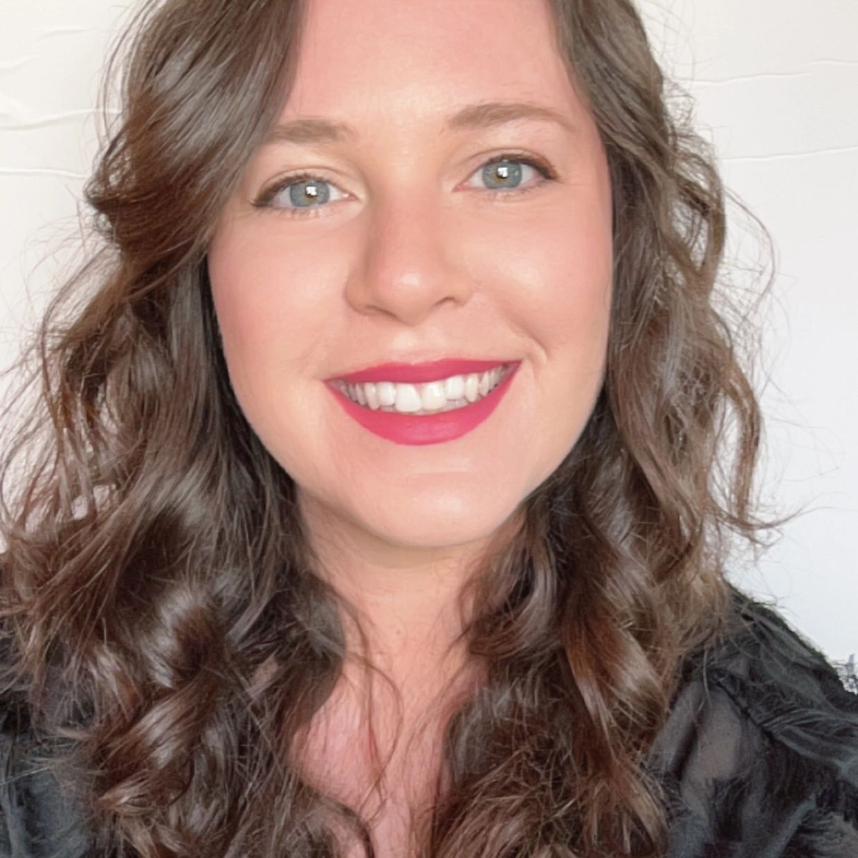 Smiling woman with curly brown hair and bright lipstick.