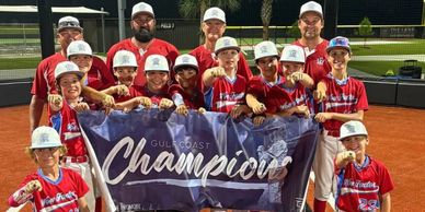 Youth baseball team proudly holding a Gulf Coast Champions banner on the field.