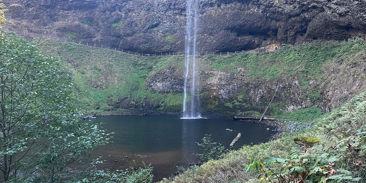 A tall waterfall cascading into a serene pool surrounded by greenery and rocky cliffs.