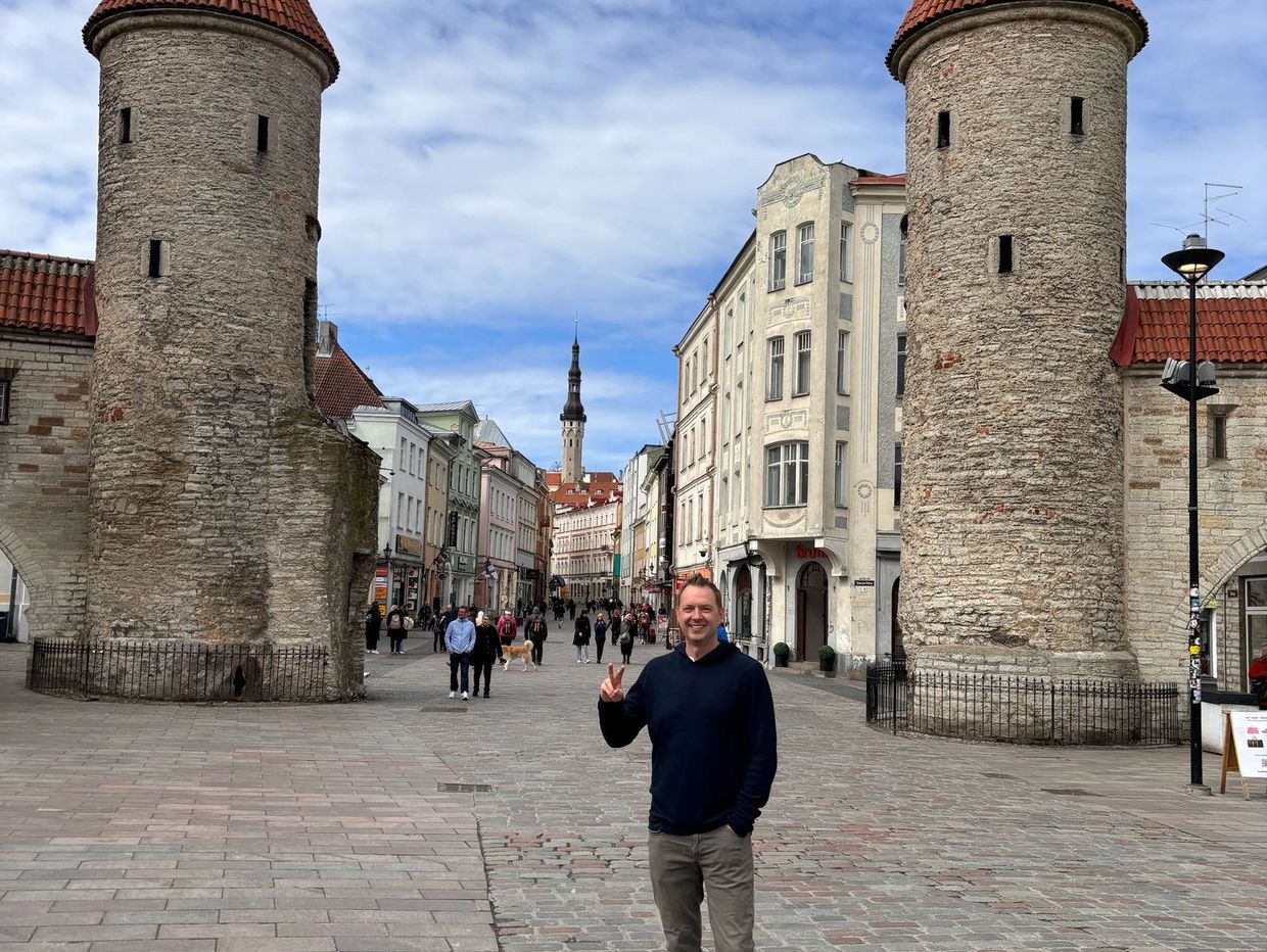A man posing with peace sign in a historic town square with stone towers.
