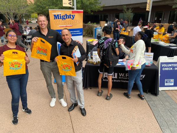 People holding yellow bags at a community event for education and volunteer check-in.
