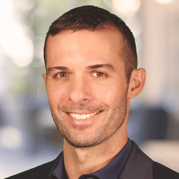Professional headshot of a smiling man in a suit with a blurred background.