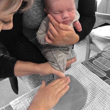 Baby being held in mums arms having a clay foot imprint taken 