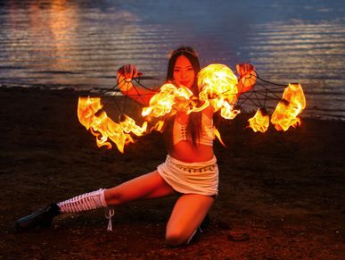 A woman performs a fire dance by the water at night.