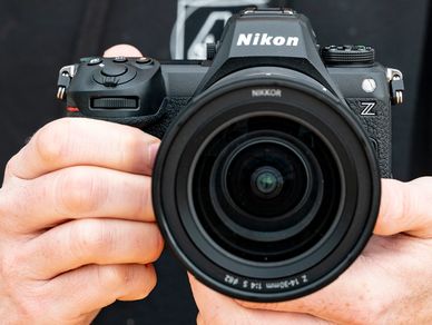 A person holding a Nikon Z series camera with a large lens.