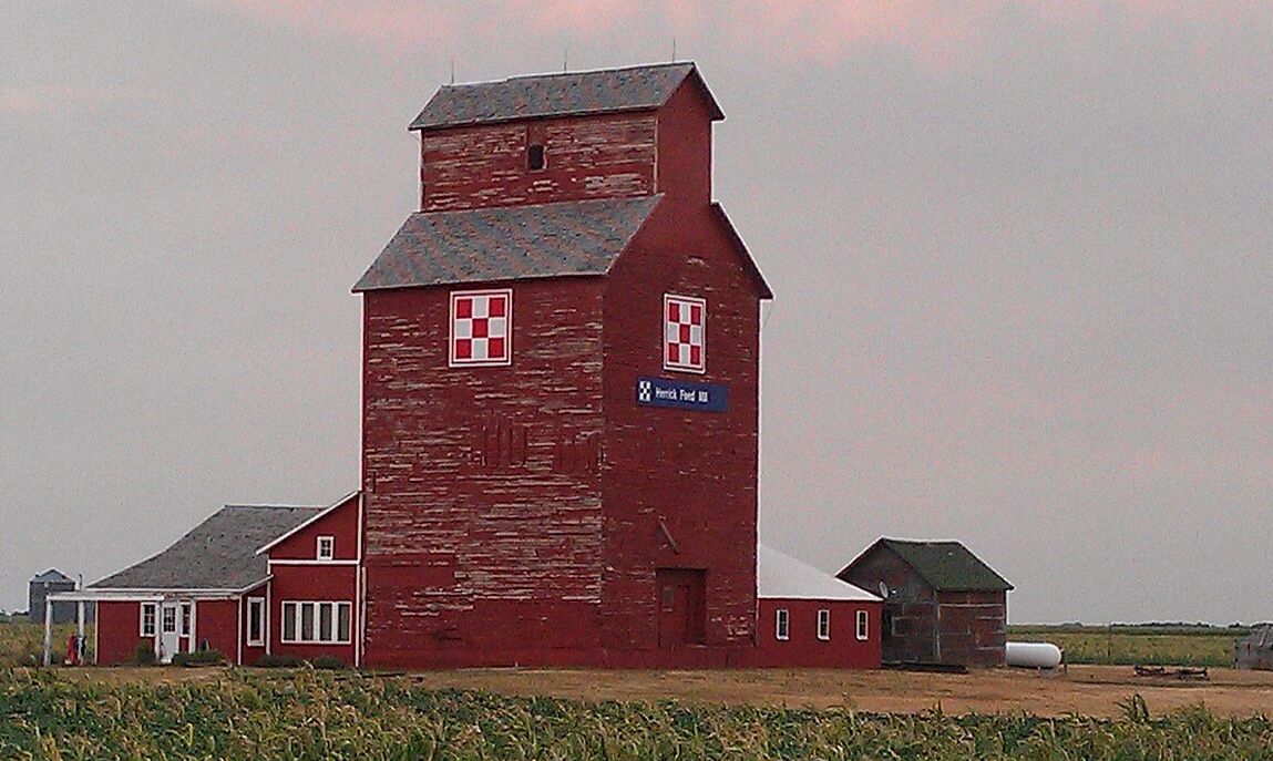 Red grain elevator in a rural field at dusk.