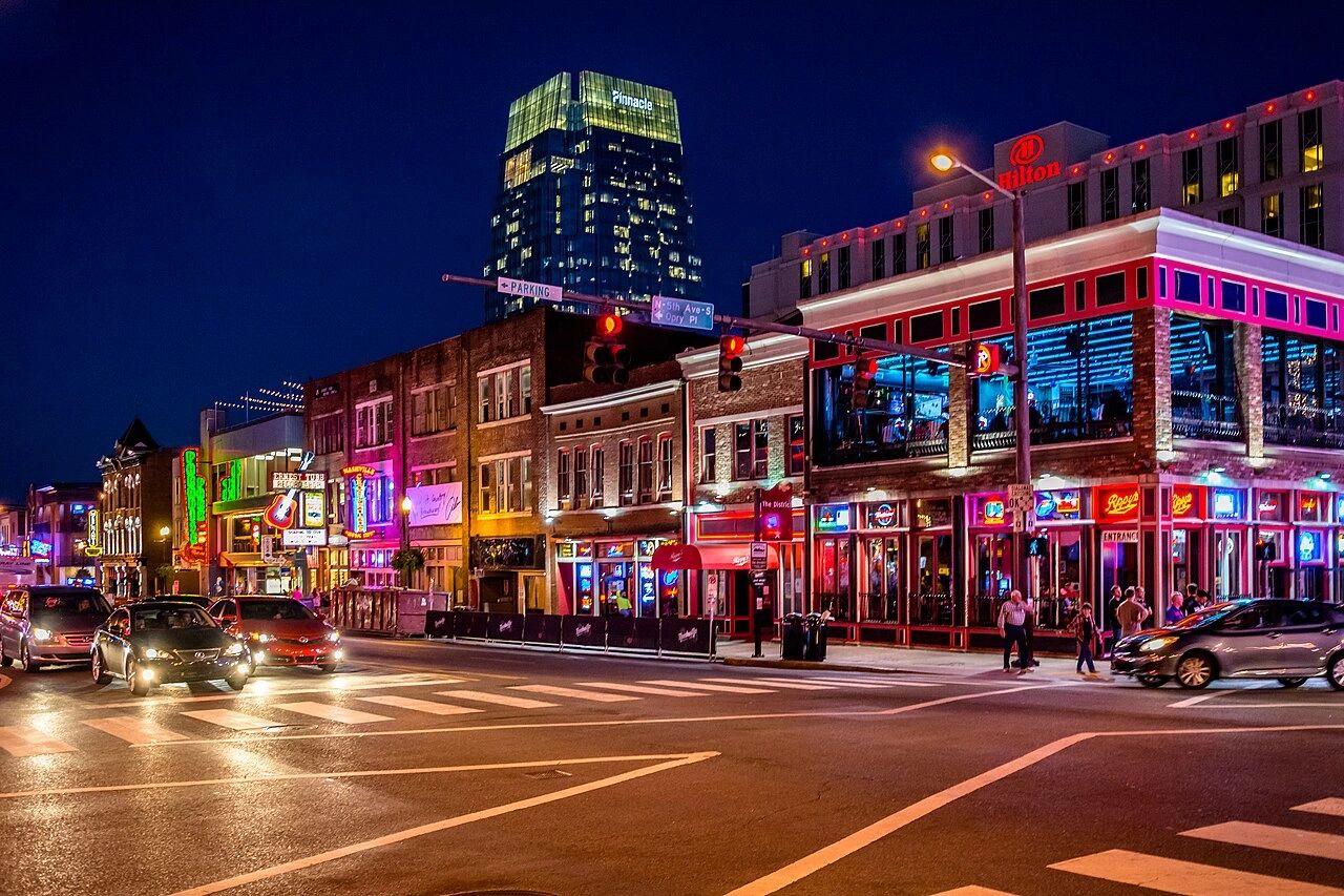 Vibrant city street at night with neon lights and lively nightlife.
