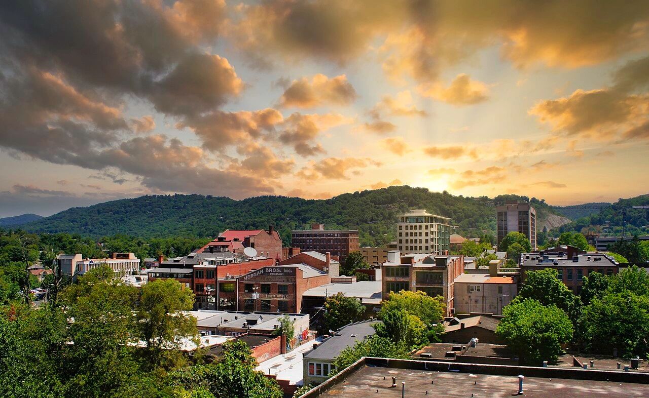 Sunset over a small city with lush green hills in the background.