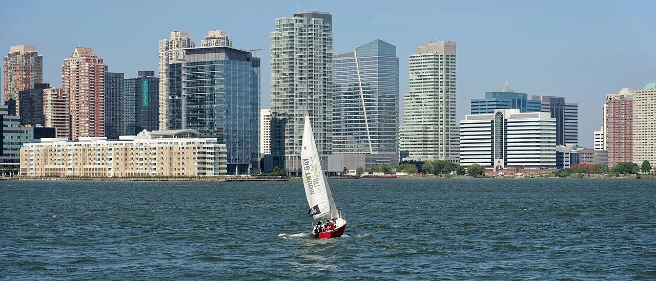 A small sailboat on water with a city skyline in the background.