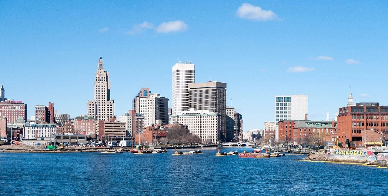City skyline with buildings along a river under a clear blue sky.
