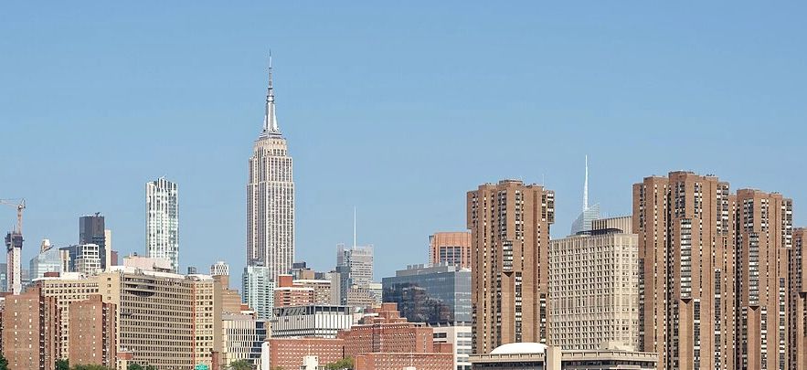 City skyline with tall buildings by the water under a clear sky.