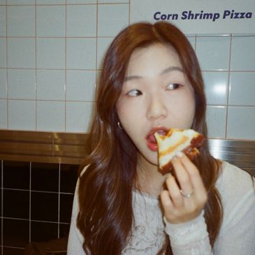 A woman eating a slice of corn shrimp pizza indoors.