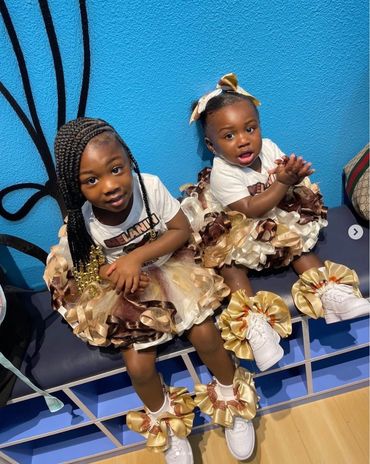 Two young girls in matching frilly brown and cream dresses sitting on a bench.