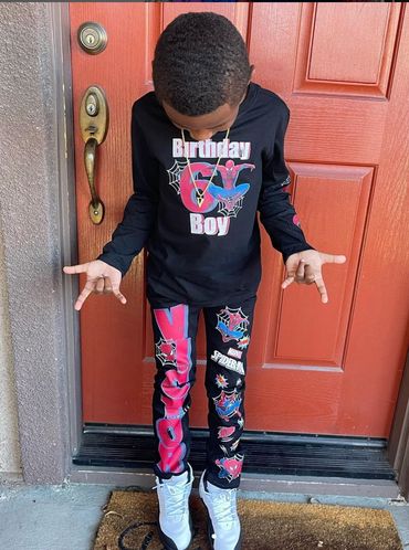 Young boy in Spider-Man themed birthday outfit standing by a red door.