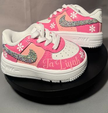 Custom pink and white Nike sneakers with rhinestone swooshes and snowflake designs.