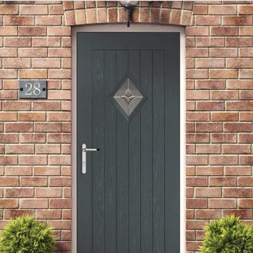 A dark gray front door with a diamond-shaped window in a brick house.