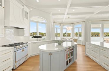 Bright kitchen with white and light blue cabinetry overlooking water.