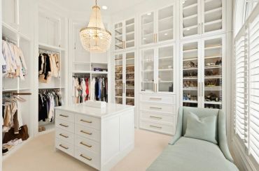 Elegant walk-in closet with white cabinetry and a chandelier.