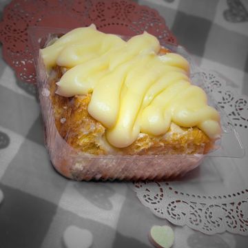 A creamy dessert topped with thick yellow icing in a plastic container.