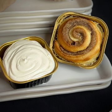 A cinnamon roll with cream cheese frosting in golden containers.