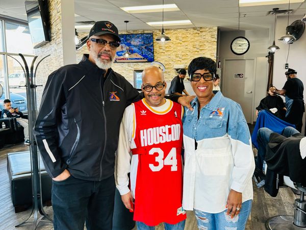 Three adults smiling and posing together in a barbershop.