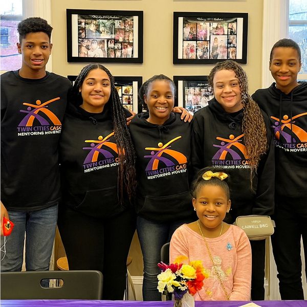 A group of smiling youth wearing matching mentoring program hoodies.