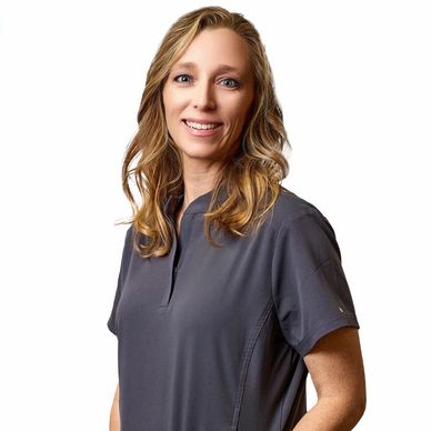 Smiling woman with wavy blonde hair in a dark gray top against a white background.