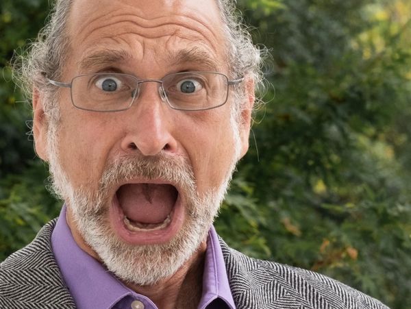 Surprised elderly man with glasses outdoors, mouth wide open.