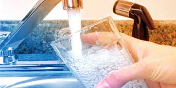 Hand filling a glass with water from a kitchen faucet.