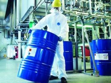 Worker in protective suit handling a hazardous chemical barrel.