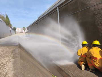 Two firefighters in yellow gear spraying water, creating a rainbow in the mist.