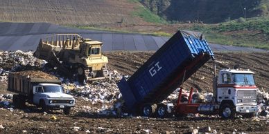 Heavy machinery and trucks unloading waste at a landfill site.